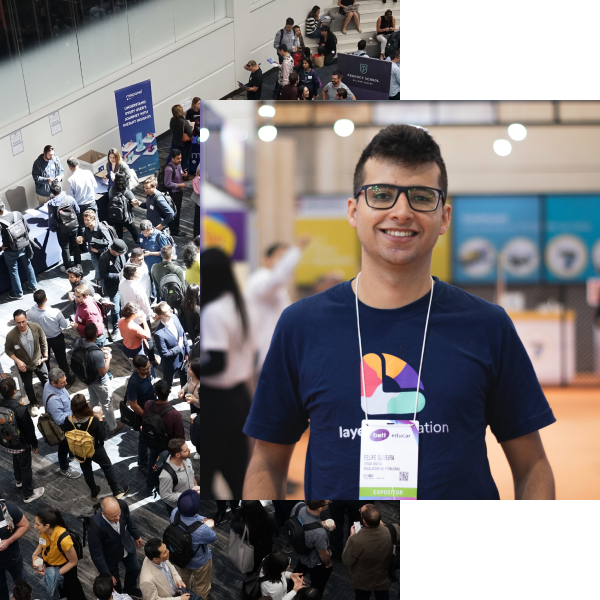 Smiling young man wearing glasses and a navy blue t-shirt with a colorful logo, standing indoors at a busy event with people and booths in the background.