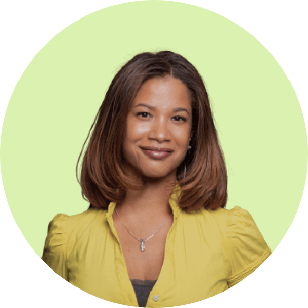 Smiling woman with shoulder-length brown hair wearing a yellow blouse and a pendant necklace against a bright green background.