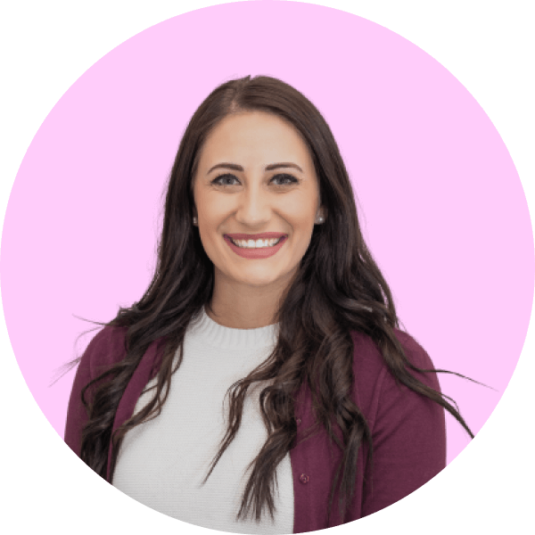 Smiling woman with long dark hair wearing a white top and maroon cardigan against a pink background.