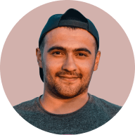 Portrait of a young man wearing a backward dark cap and a gray shirt, smiling softly.