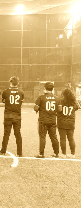 Three people standing on a sports field facing away, wearing black jerseys with names and numbers: Vinay 02, Suman 05, and an unnamed person 07.