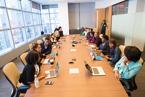 Diverse group of people seated around a long conference table with laptops, engaged in a meeting in a modern office.