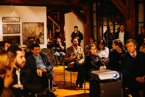 Group of people engaged in a discussion in a cozy room with wooden beams and framed artwork on the walls.