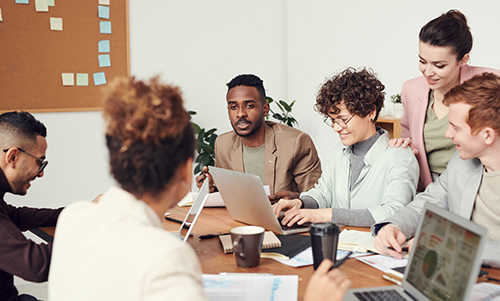Diverse group of five colleagues collaborating around a table with laptops and documents in a modern office.