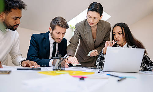 Four diverse professionals collaborating around a table with documents and a laptop in a modern office.