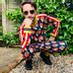 Person crouching outdoors on stone steps wearing a colorful checkered jacket, black pants, and sunglasses.