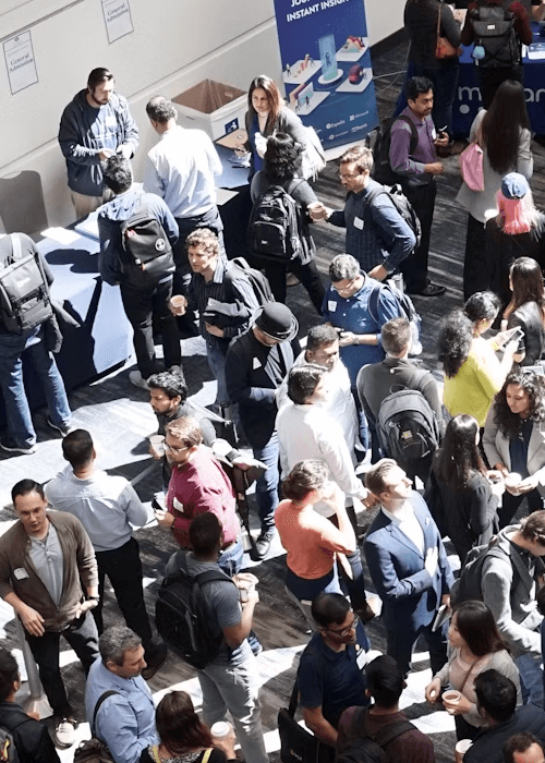 Crowd of people socializing and standing with drinks at a networking event or conference.