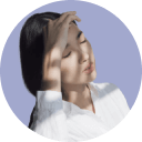 Young woman with closed eyes touching her forehead, appearing thoughtful against a lavender background.