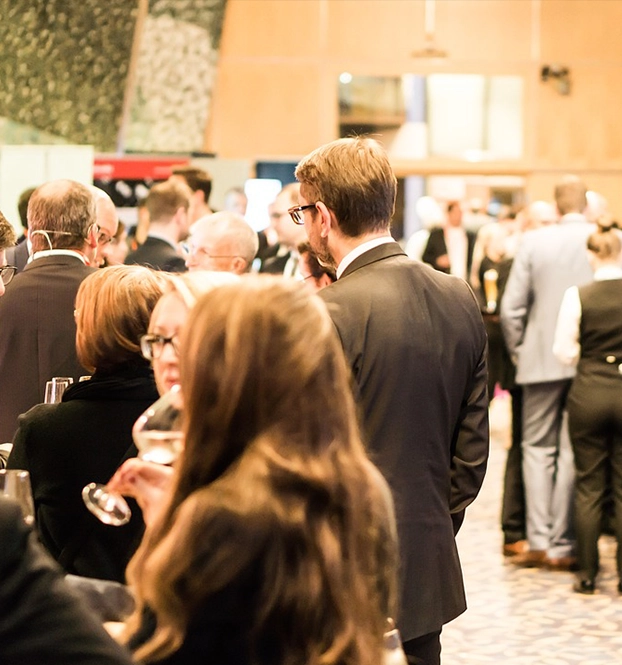 People dressed in formal attire mingling and holding drinks at an indoor social event.