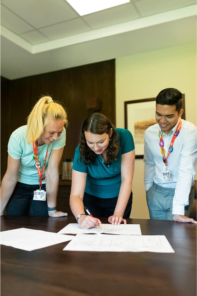 Three colleagues reviewing and marking documents spread on a table in a meeting room.