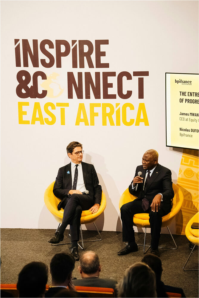Two men in business suits seated on yellow chairs speaking at Inspire & Connect East Africa event with audience in foreground.